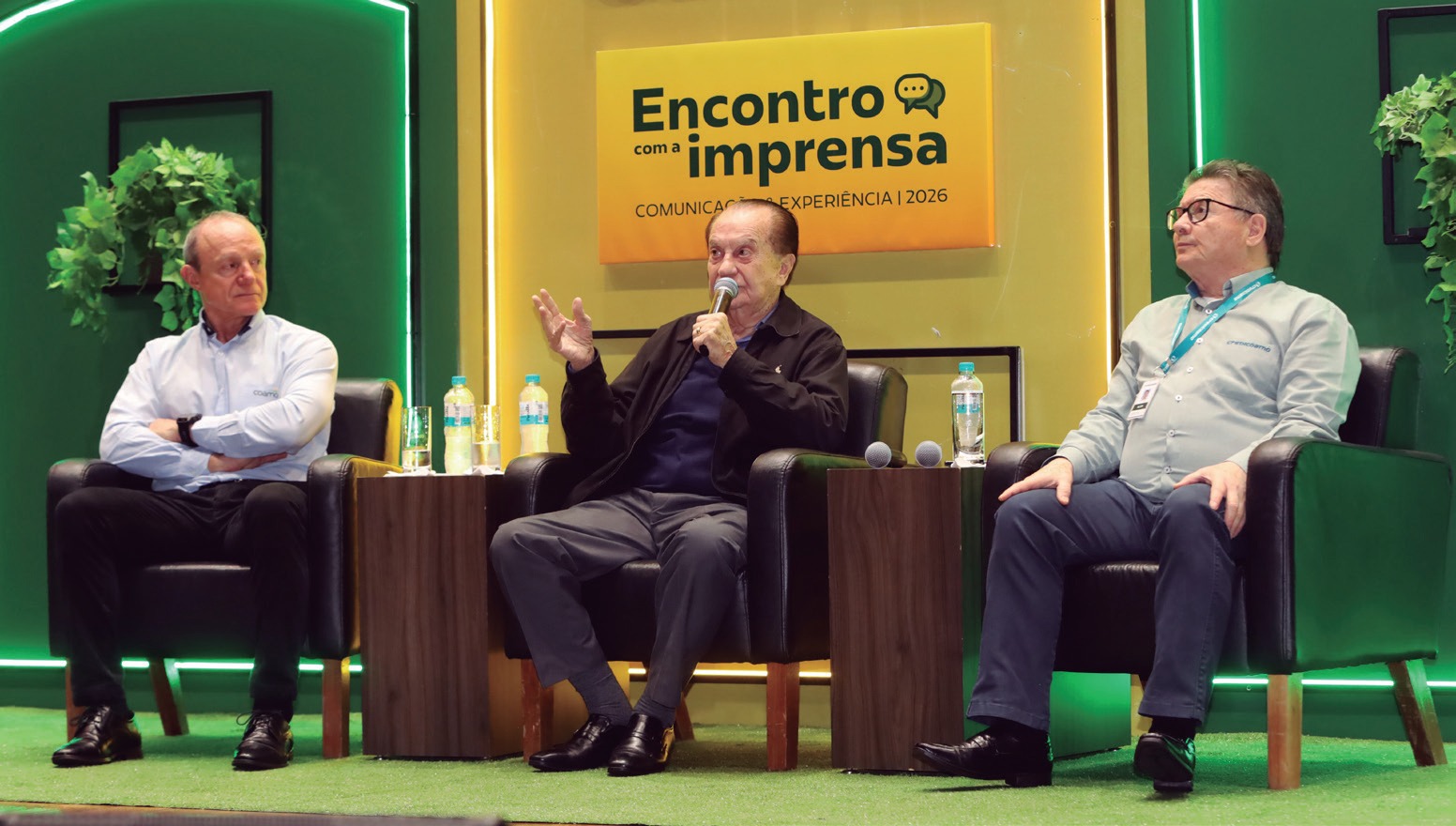 Tr&ecirc;s homens sentados em poltronas no palco do Encontro com a Imprensa, um deles falando ao microfone