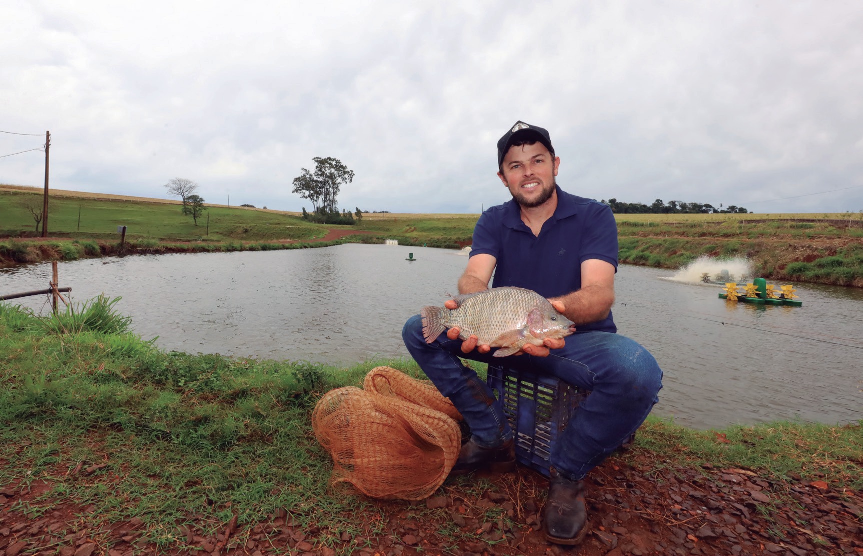 Cooperado J&uacute;lio Cesar Pauli segurando uma til&aacute;pia &agrave; beira de um tanque de cria&ccedil;&atilde;o