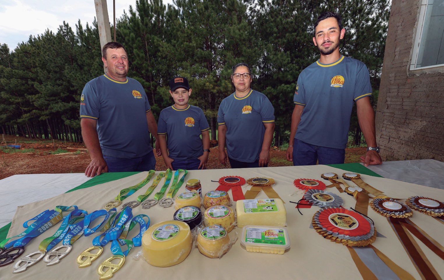 Fam&iacute;lia em p&eacute; atr&aacute;s de mesa com queijos, medalhas e fitas de premia&ccedil;&atilde;o