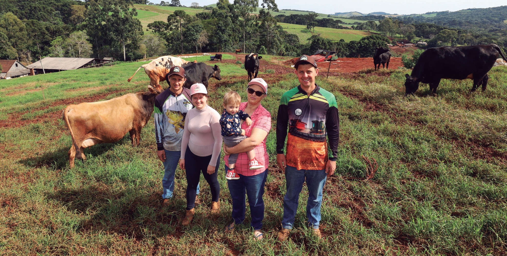 Fam&iacute;lia em p&eacute; numa pastagem, com vacas ao fundo