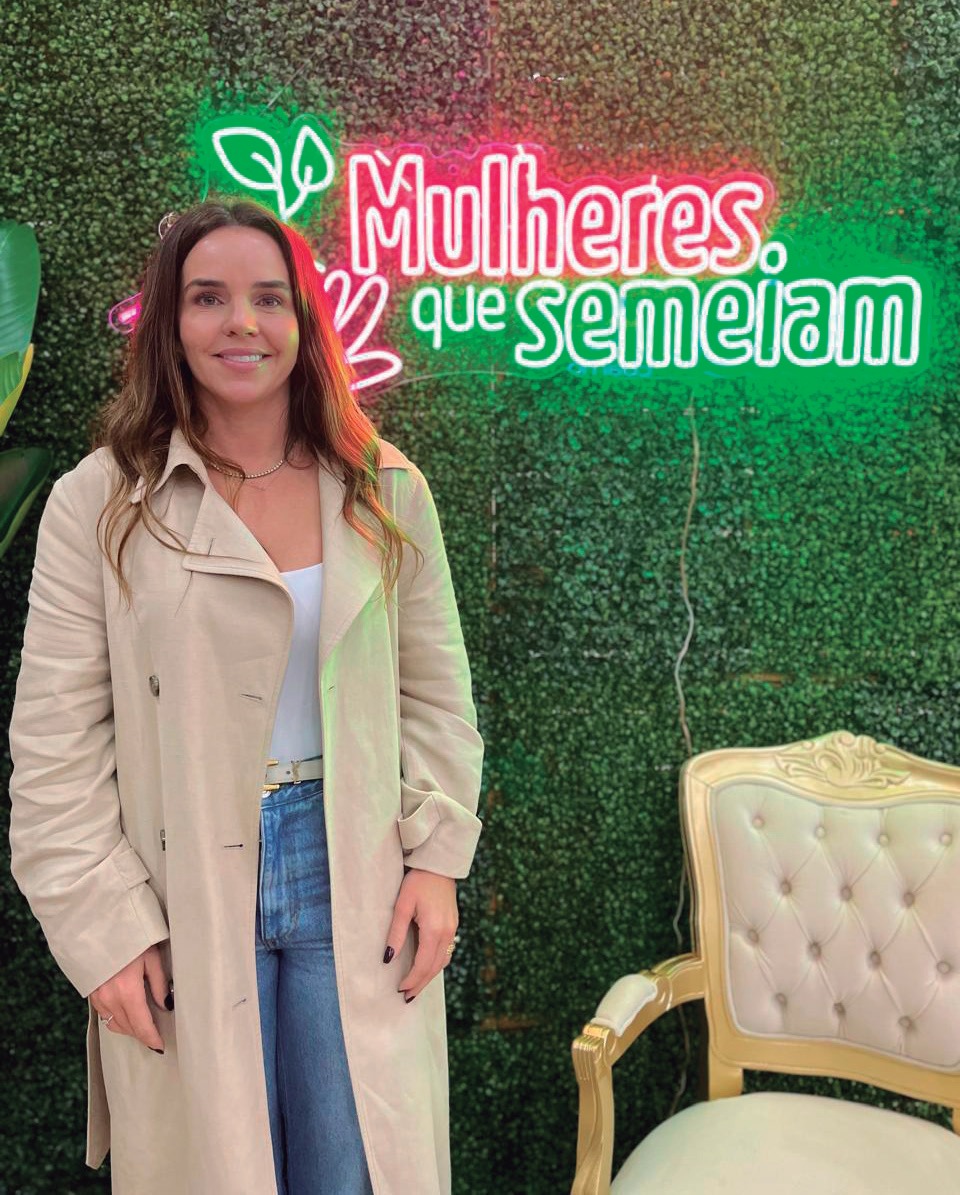 Tenile Lovo Ferronatto em frente a um painel do evento Mulheres que Semeiam