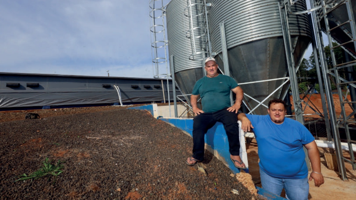 Cooperados em Ipuaçu, Adir e Luiz Fernando Spada, em frente a um aviário e silos de armazenamento.