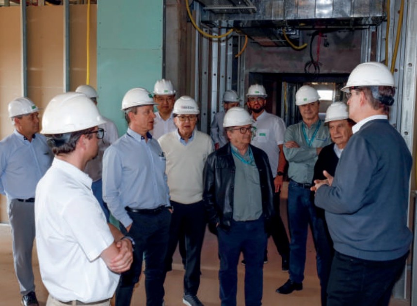 Diretores com capacetes de segurança dentro da obra do hospital, ouvindo explicações.