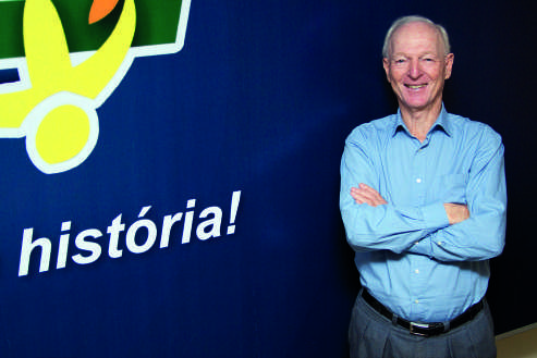 Guntolf van Kaick sorrindo com os braços cruzados em frente a um painel azul com a palavra 