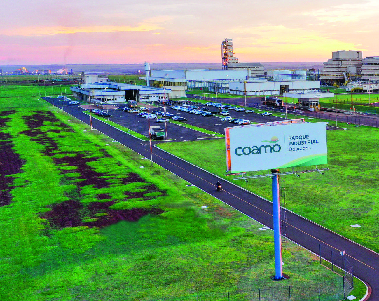 Vista aérea do parque industrial da Coamo em Dourados, com um grande outdoor da Coamo em primeiro plano.