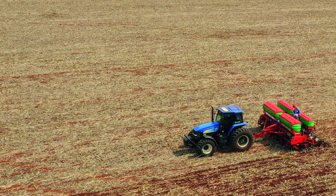 Plantio sendo realizado com trator azul e plantadeira vermelha.