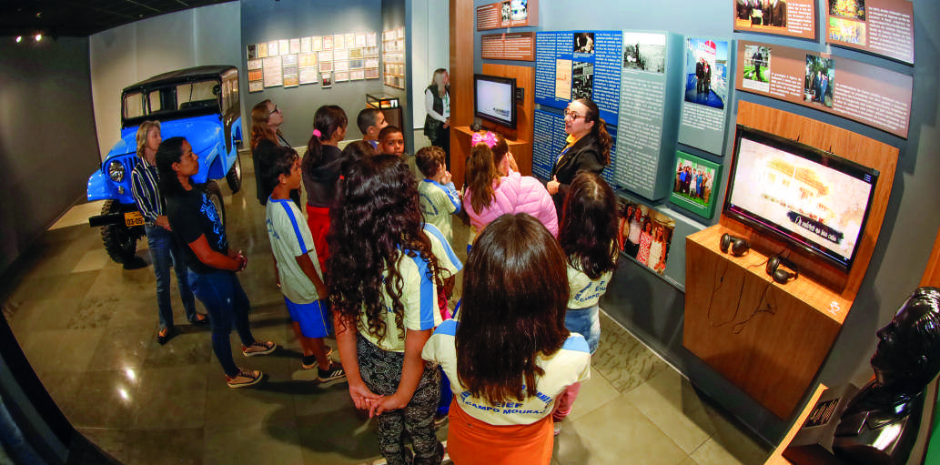 Visitantes, incluindo um grupo de estudantes, observam as exposições no Memorial Coamo.