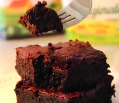 Um pedaço de brownie em um garfo, com mais brownies ao fundo.