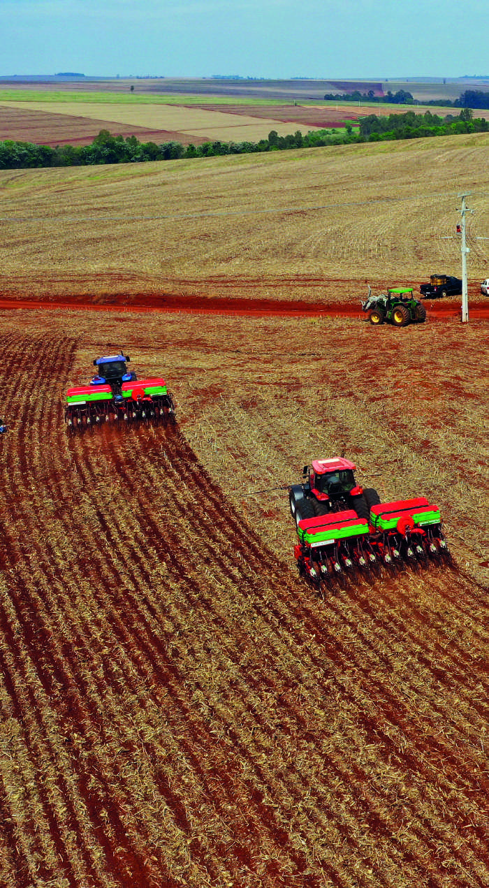Vista aérea de tratores realizando o plantio em campo arado.